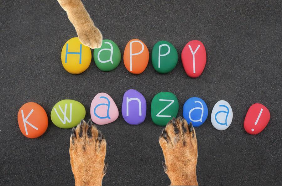 Colorful stones spelling out "Happy Kwanzaa!" framed by two dog paws and one cat paw.